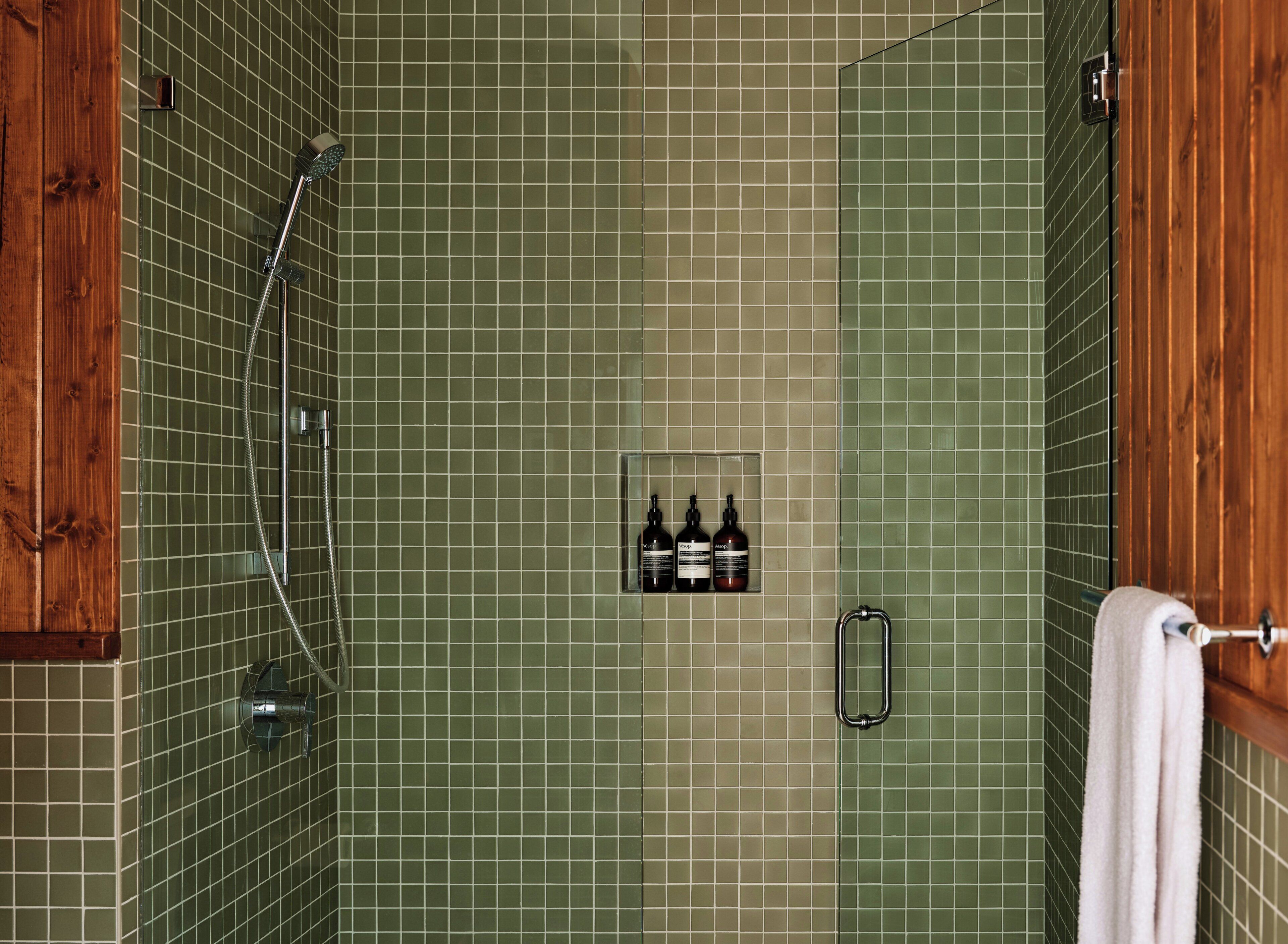 Un baño con paredes de azulejos verdes, una puerta de madera, un perchero y una estantería con botellas.