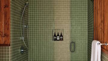 Un baño con paredes de azulejos verdes, una puerta de madera, un perchero y una estantería con botellas.