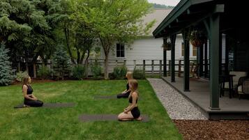 Two individuals seated on yoga mats in a grassy outdoor area with a building in the background.