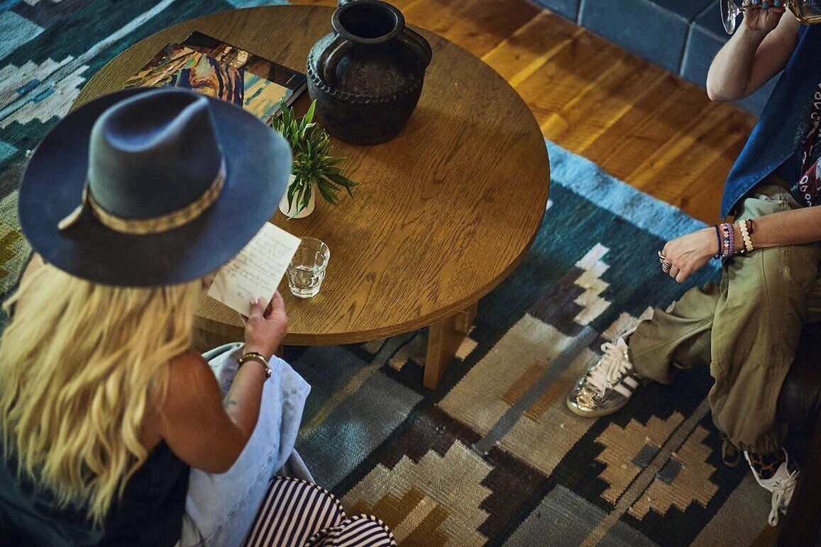 Une table ronde en bois, avec une personne tenant un menu, une autre personne assise en face, et une petite plante posée sur la table.
