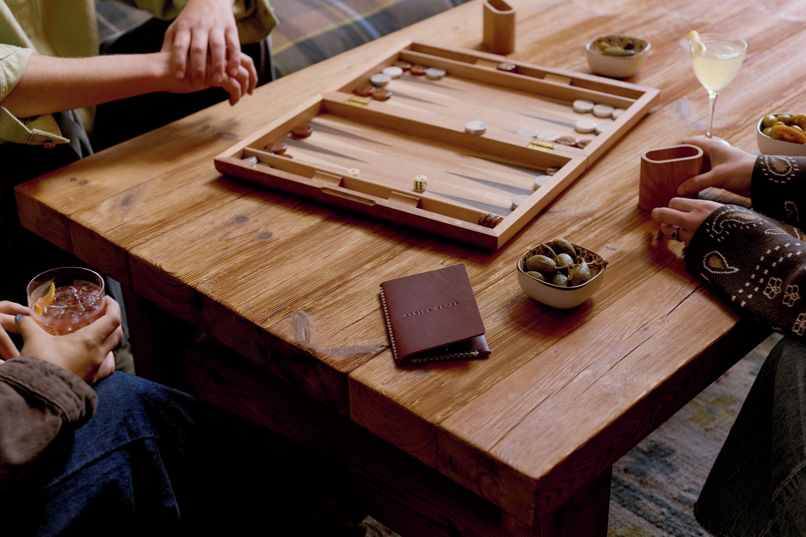 Uma mesa de madeira com um jogo de tabuleiro, um copo de bebida e uma carteira de couro.
