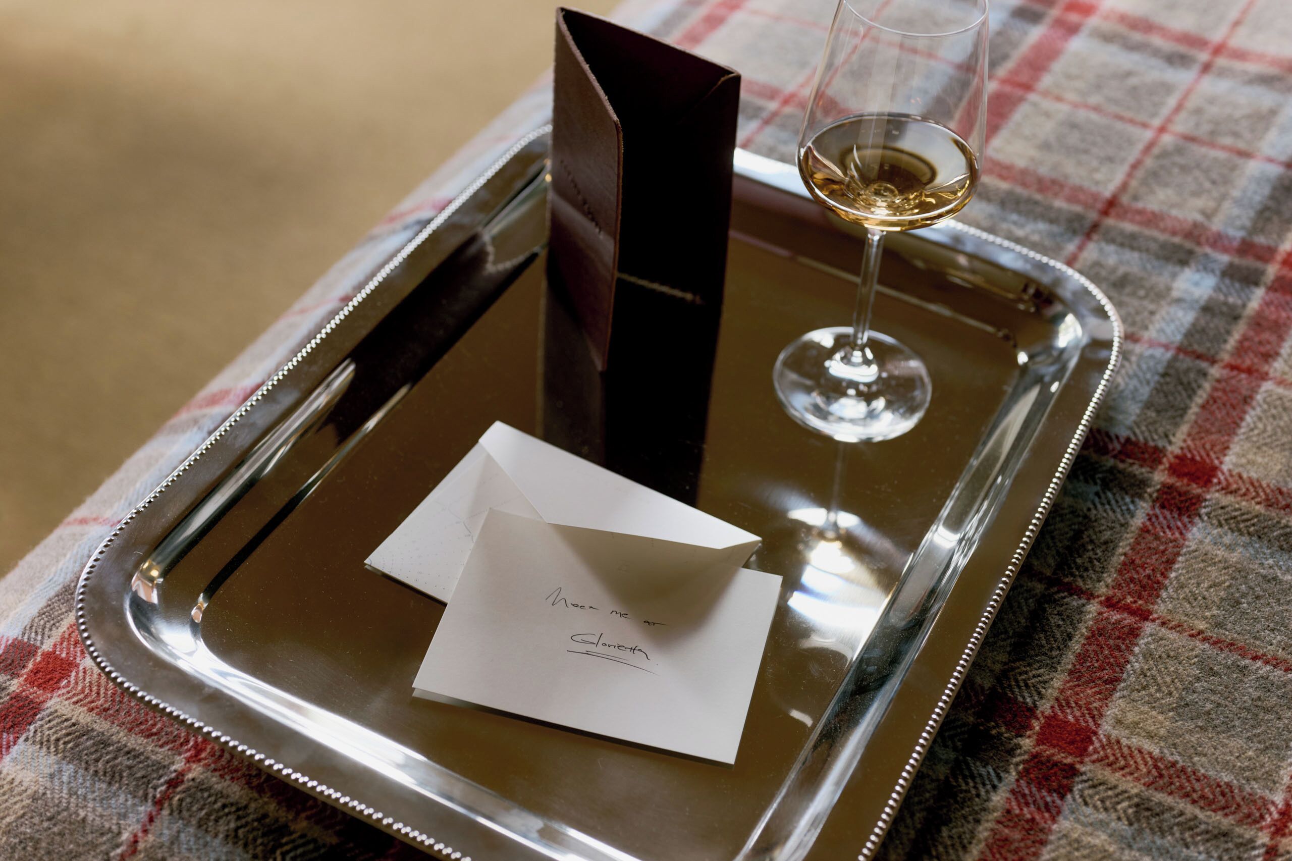 A tray with a glass of wine, a menu, and a card on a checkered tablecloth.