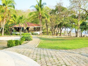 Un chemin pavé mène à un bâtiment doté d’un toit en tuiles, entouré d’une végétation luxuriante et de palmiers.