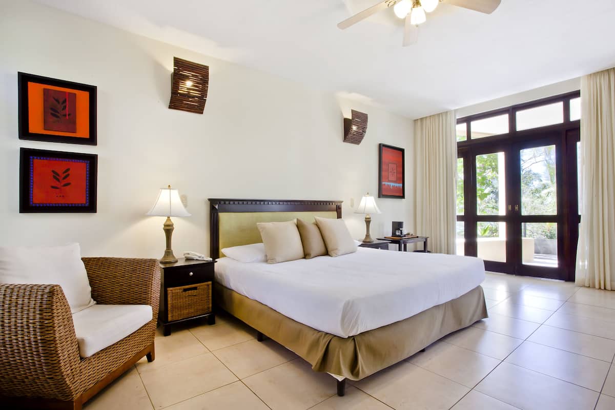 A hotel room with a large bed, a wicker sofa, two bedside tables with lamps, and framed artwork on the walls.