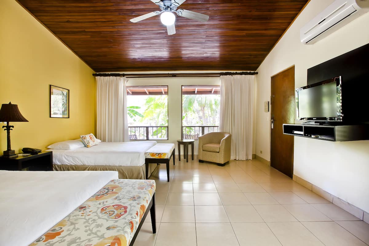 A hotel room with two beds, a ceiling fan, a TV, and a balcony with curtains.