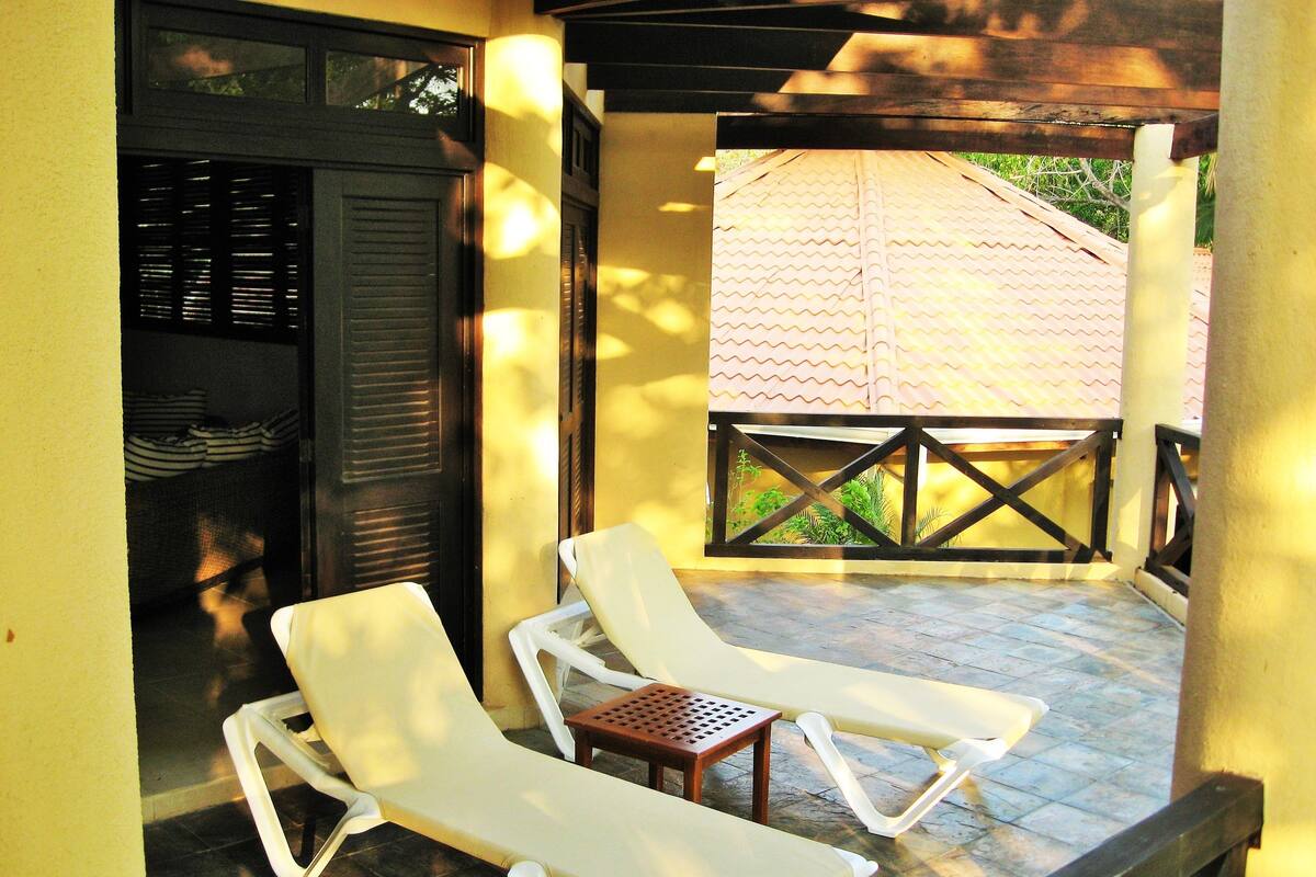 A covered outdoor seating area with two white lounge chairs and a small table.
