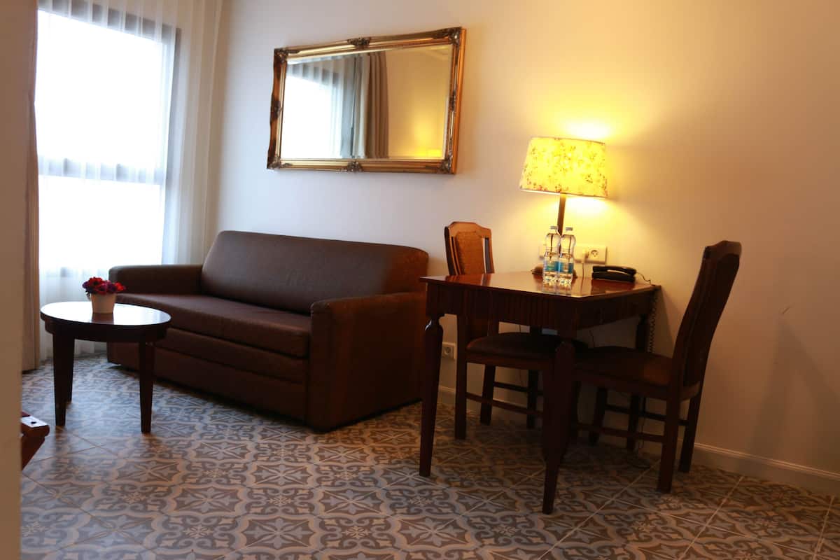 Una habitación con un sofá, una mesita de noche con lámpara, una silla y un espejo en la pared.