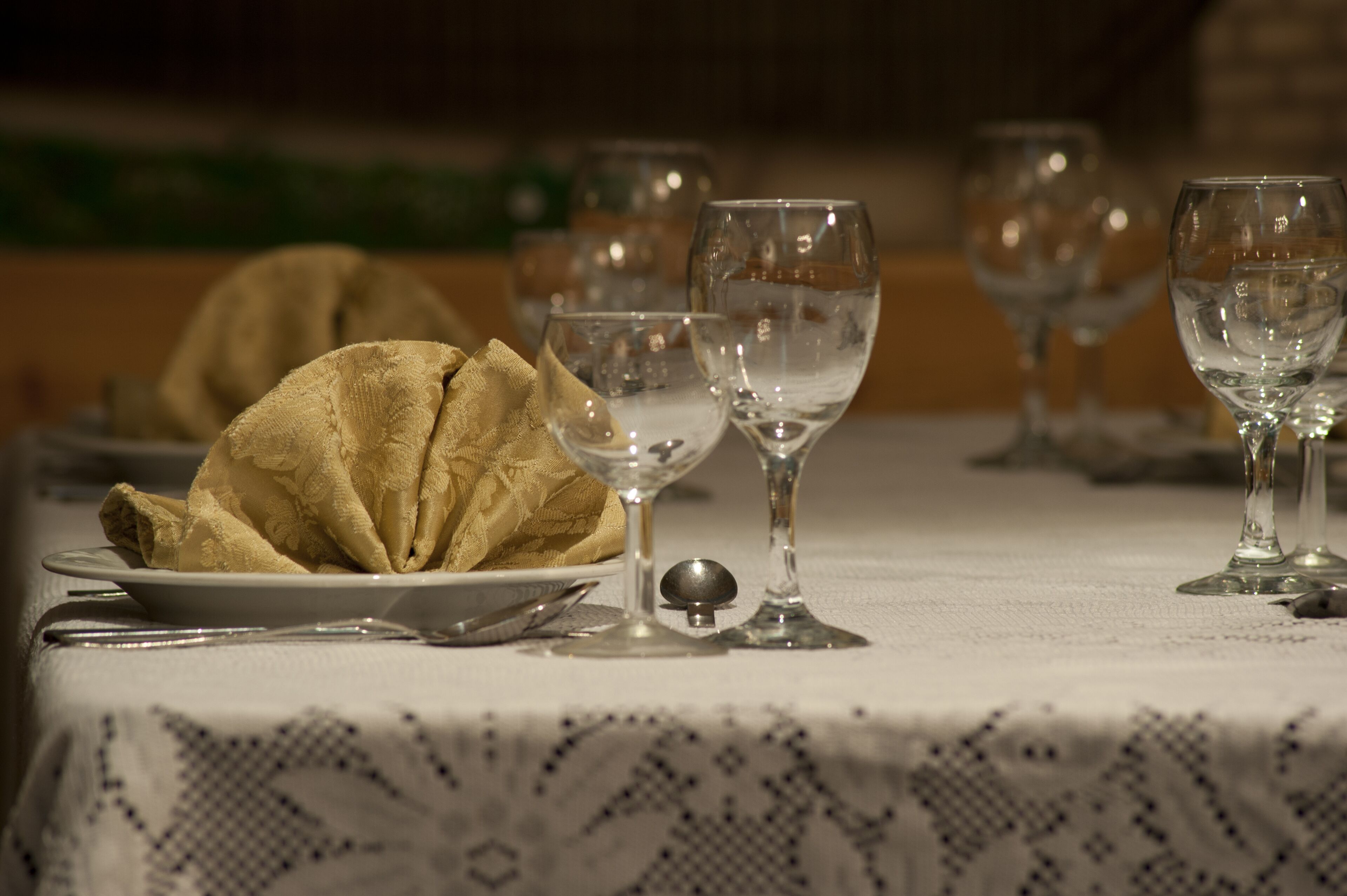 Uma mesa posta com uma toalha de tecido dobrada, um prato e várias taças de vinho.