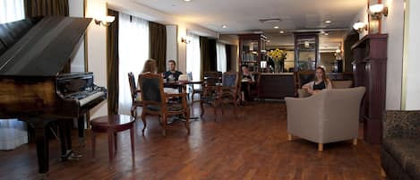 A spacious living room with a grand piano, comfortable seating, and a well-lit area with a bar and kitchen in the background.