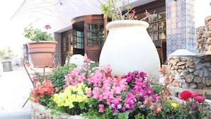 A flower bed with various colorful flowers in front of a building with a tiled facade and a stone wall. - Jerusalem Gold Hotel (Jerusalem)