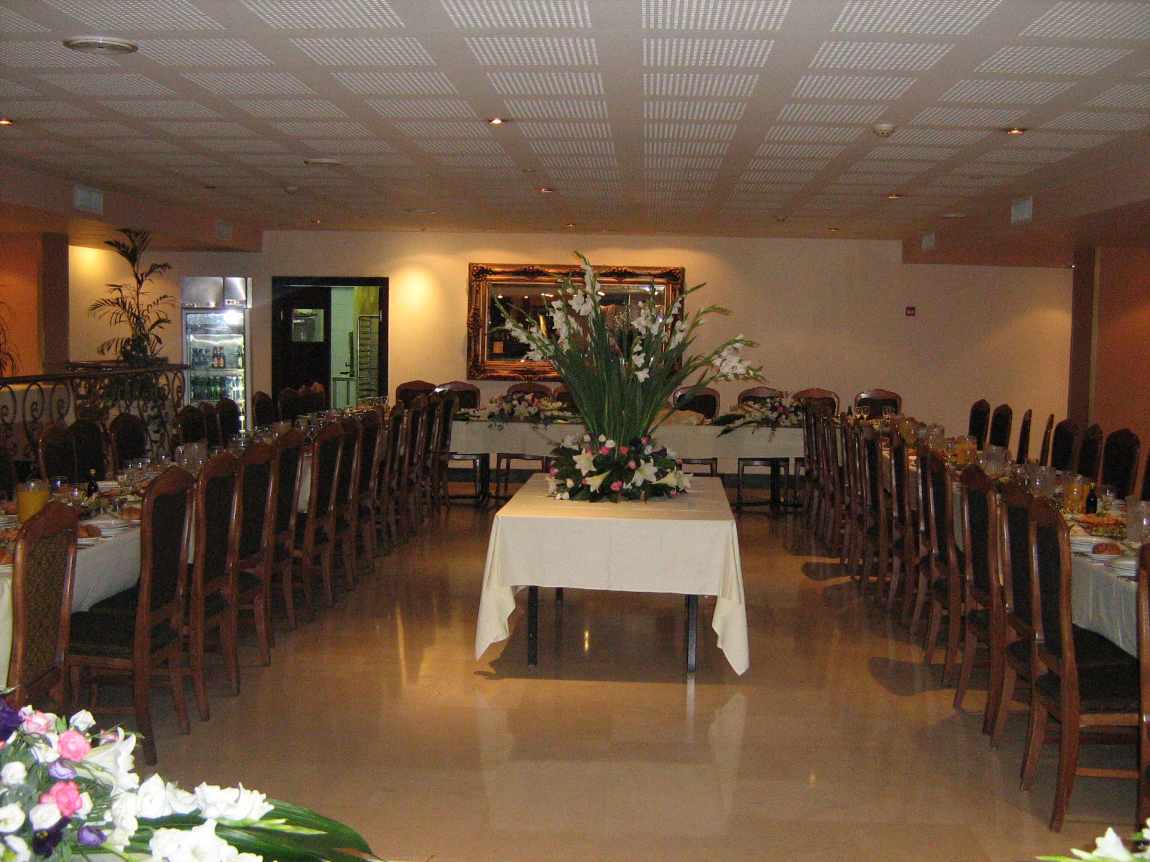 Un salón de banquetes con mesas largas, sillas y un arreglo floral central.