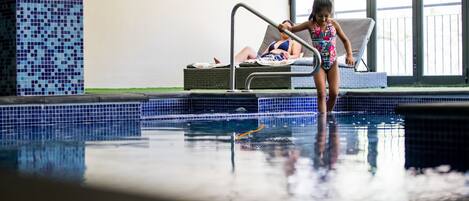 An indoor swimming pool with a tiled wall and a lounge chair.
