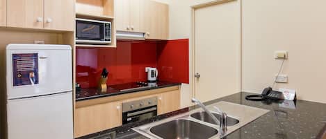 A compact kitchen with a refrigerator, microwave, stove, and sink.