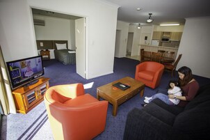Una sala de estar con televisor, sillones naranjas, un sofá y un comedor con sillas y una mesa.
