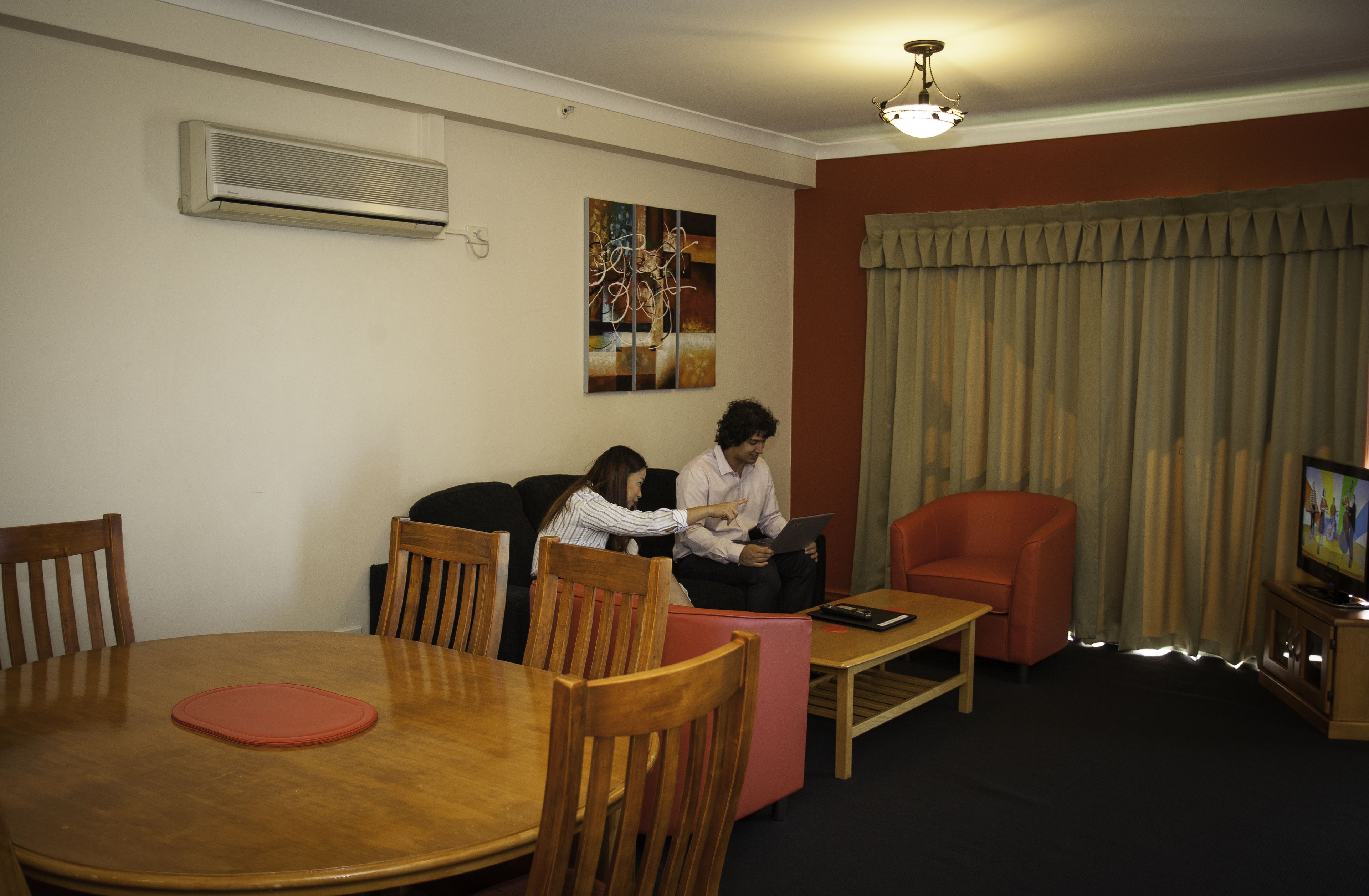 Un salon comprenant une table à manger, des chaises, un canapé, un fauteuil rouge, un téléviseur et un appareil de climatisation.