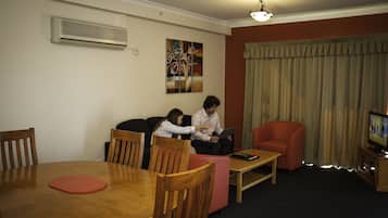 A living room with a dining table, chairs, a sofa, a red armchair, a television, and an air conditioning unit.