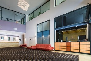 A modern hotel lobby with a reception desk, a red sectional sofa, and a patterned carpet. - Starwest Apartments Alderney on Hay (East Perth)