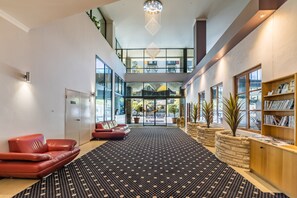 A spacious lobby with a patterned carpet, red leather sofas, a reception desk, and a bookshelf. - Starwest Apartments Alderney on Hay (East Perth)