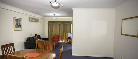 Habitació d'hotel amb taula de menjador, cadires, sofà, televisió i lluminària de sostre.