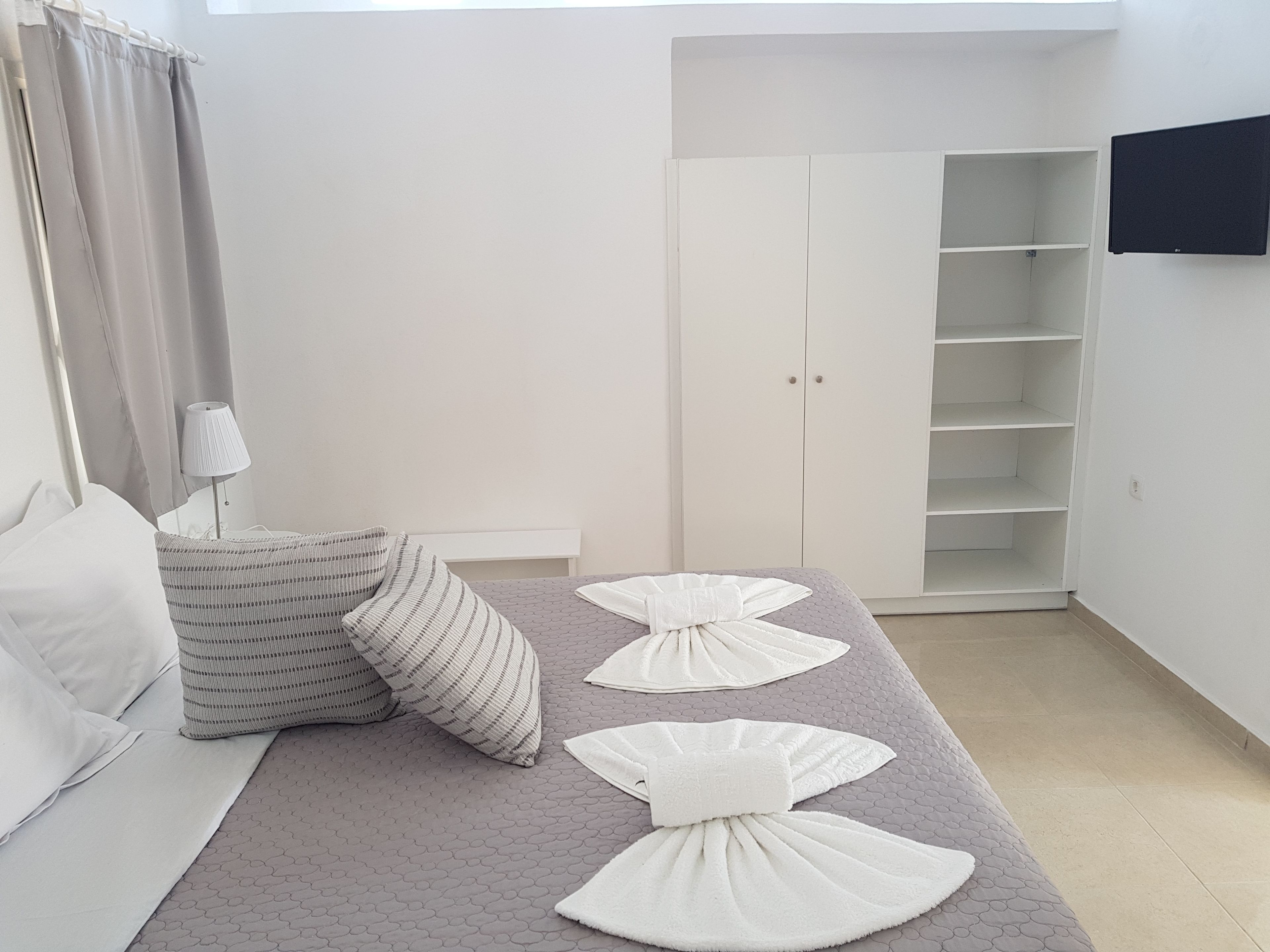 A bedroom with a bed, pillows, a lamp, a wardrobe, and a TV.