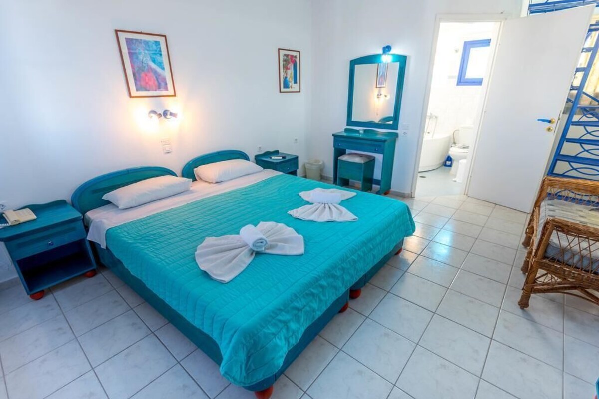A hotel room with a bed, a nightstand, a dresser, a mirror, and a bathroom visible through an open door.
