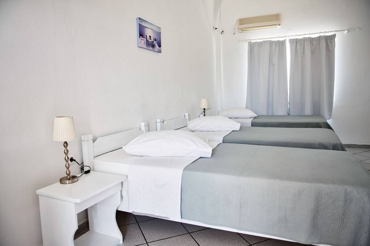 A hotel room with two beds, a bedside table with a lamp, a picture on the wall, and an air conditioning unit.