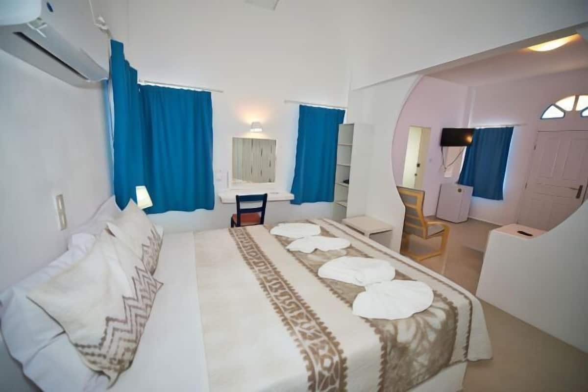 A bedroom with a bed, a desk, a chair, a mirror, and a door.