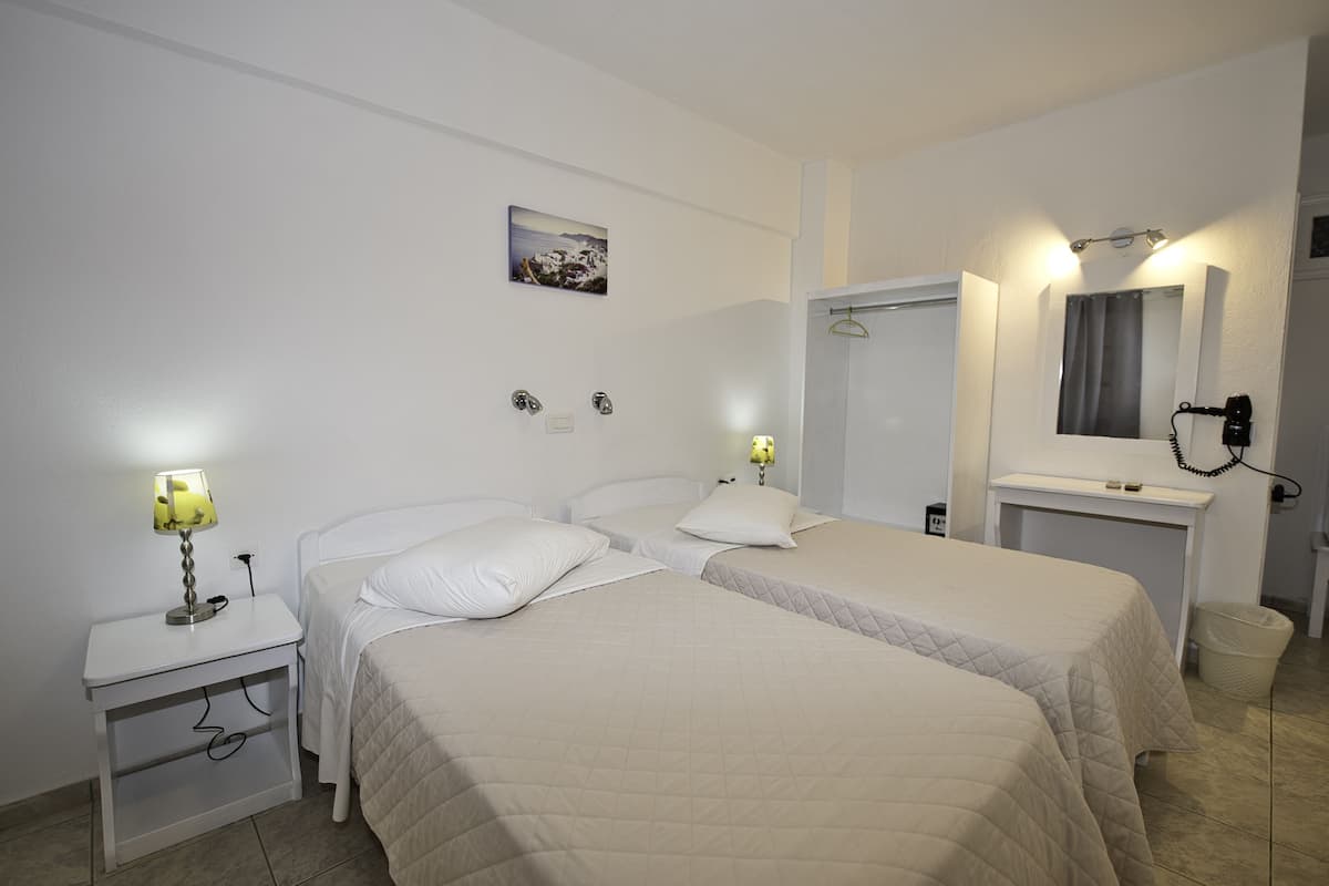 A hotel room with two beds, a nightstand with a lamp, a mirror, and a picture on the wall.