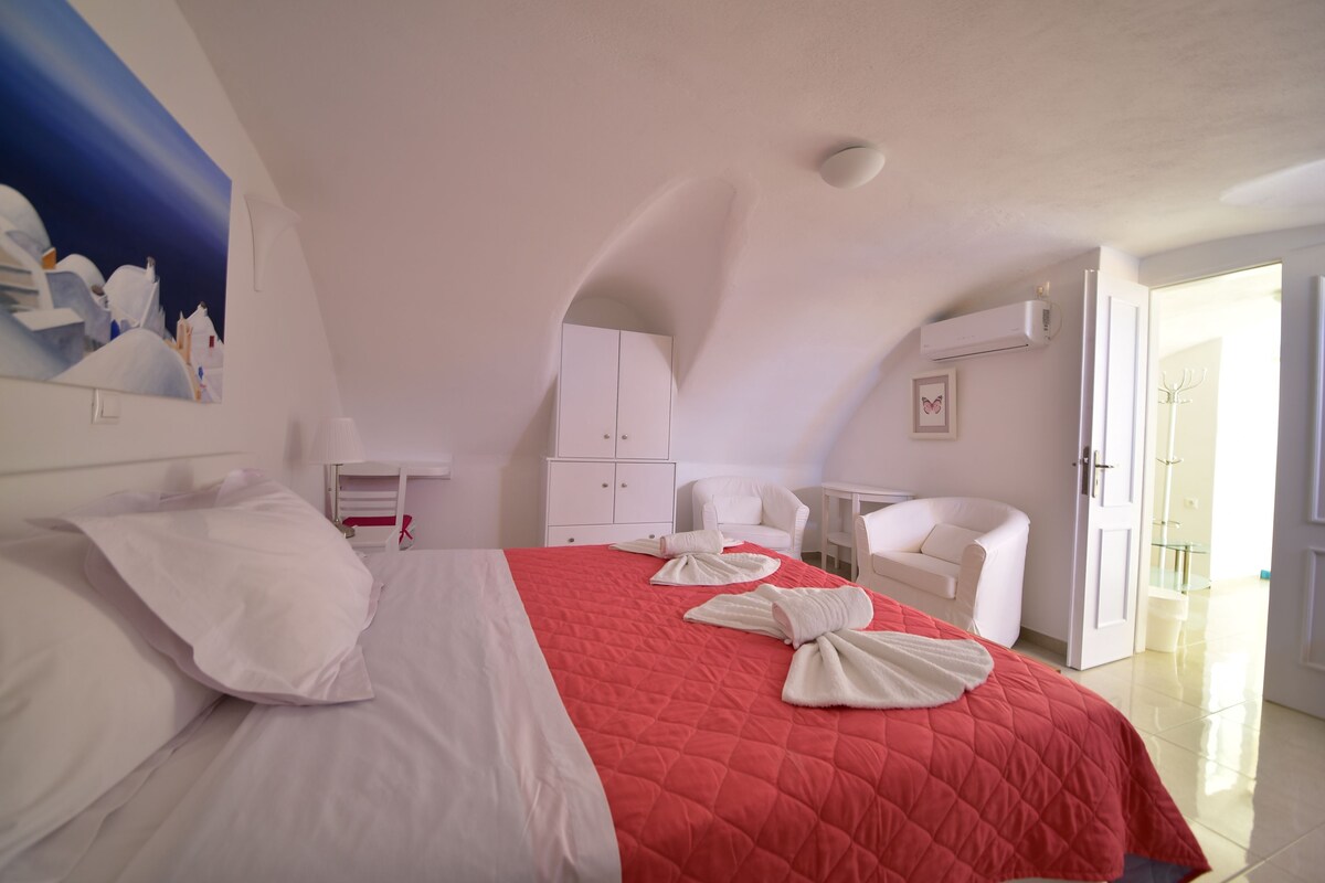 Quarto de hotel com uma cama, móveis brancos, uma mesa pequena e uma cadeira.