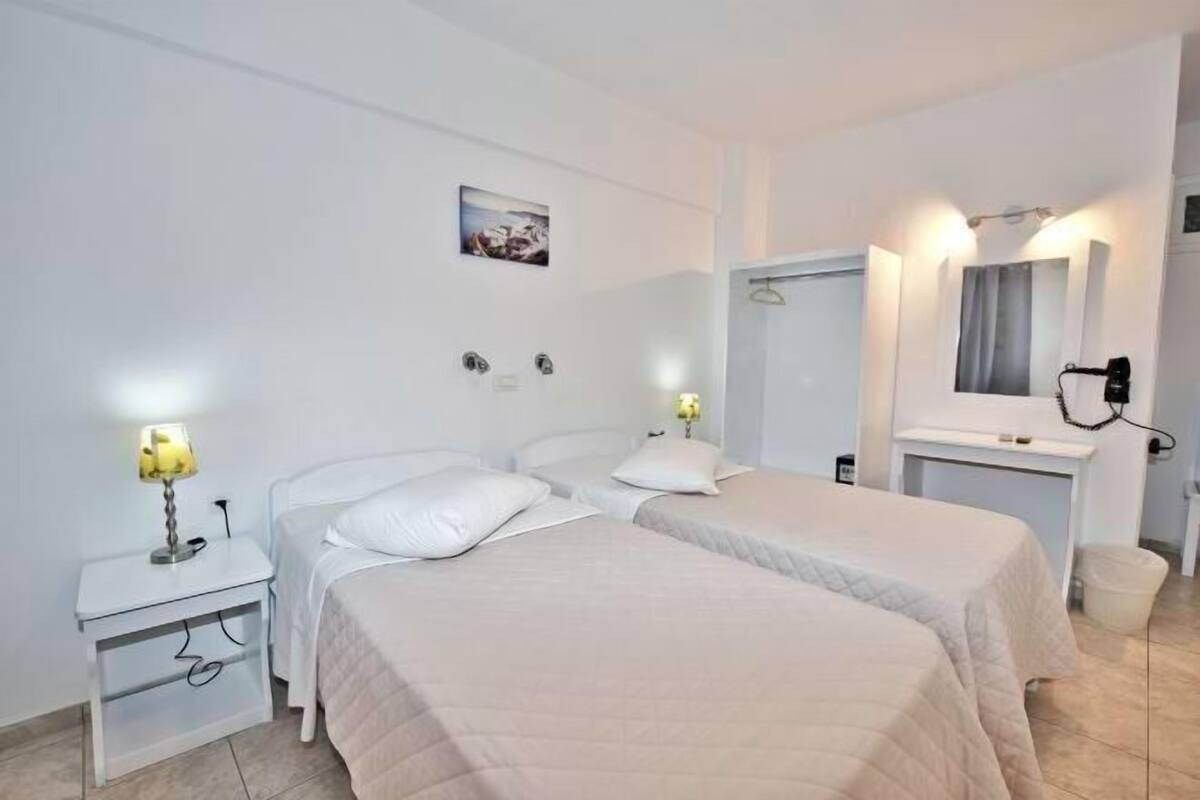 A hotel room with two beds, a bedside table with a lamp, a mirror, and a picture on the wall.