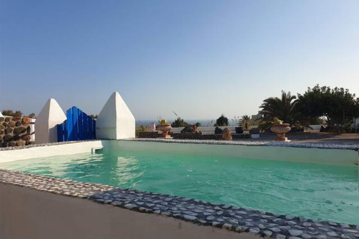 A swimming pool with a stone border, a white building with a blue door, and a clear sky.
