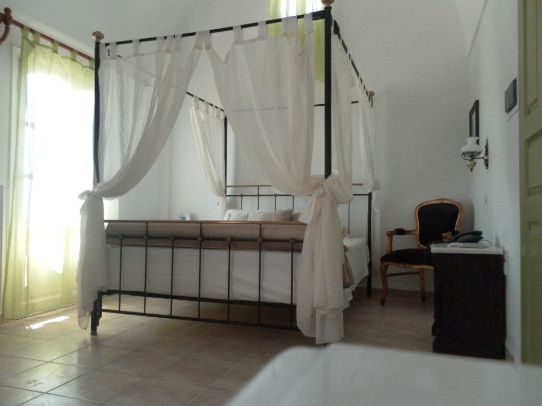 Una cama con dosel y cuatro columnas, una mesita de noche, una silla y una lámpara fijada a la pared.