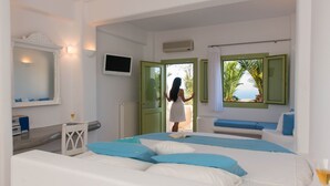 A bedroom with a bed, a window with a view, a TV, and a bedside table with a glass. - Aelia by Eltheon (Santorini)