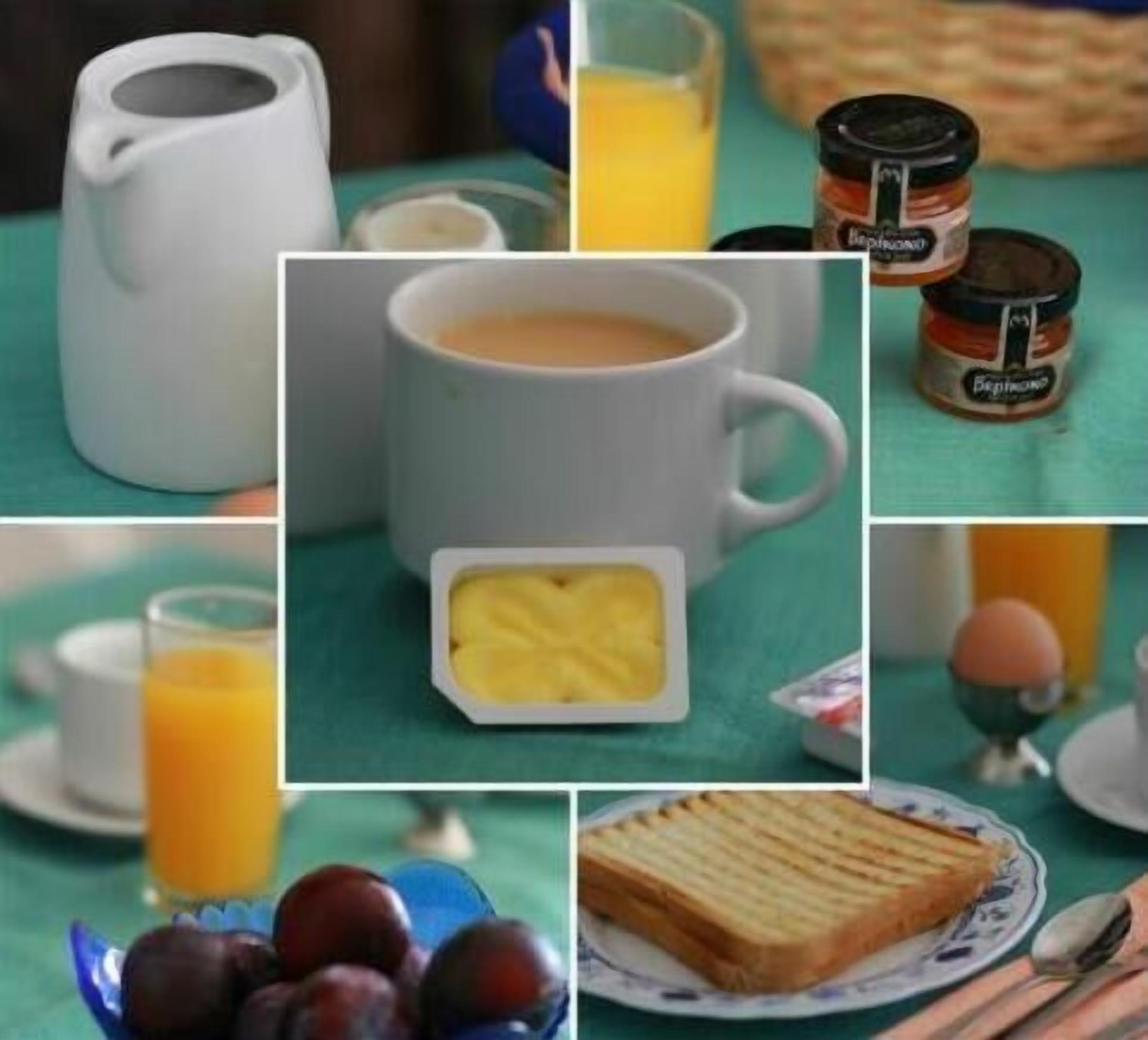 A breakfast setting with a coffee mug, a glass of orange juice, a jar of jam, a plate with a slice of bread, and a bowl of fruit.