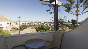 Un balcon avec une table et des chaises, donnant sur une ville côtière avec ses bâtiments et un ciel dégagé.