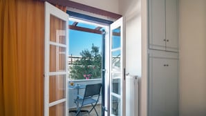 Une chambre avec une porte coulissante donnant sur un balcon, une petite table avec une chaise et une armoire blanche.