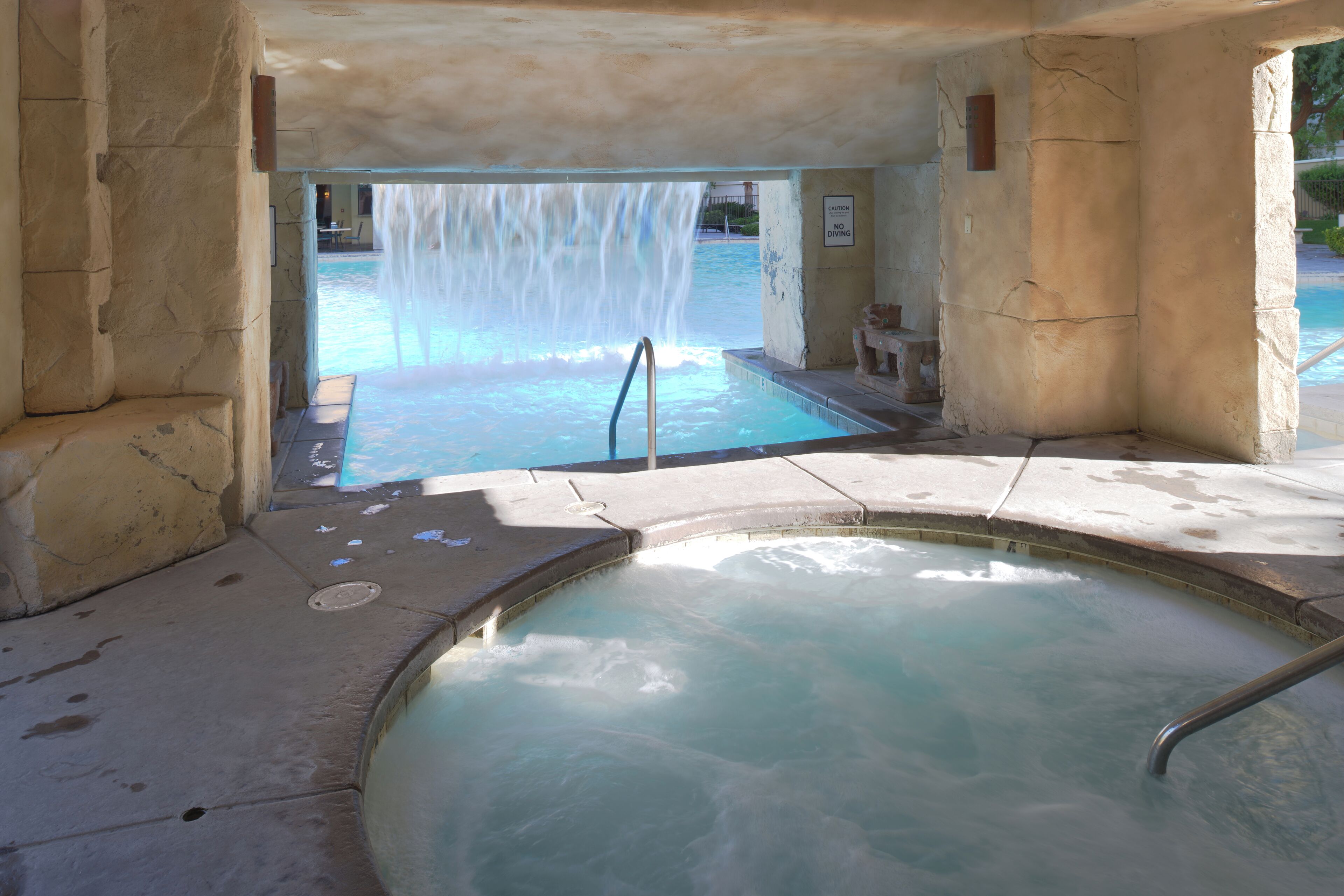 A hot tub with a waterfall feature, a pool, and a caution sign.