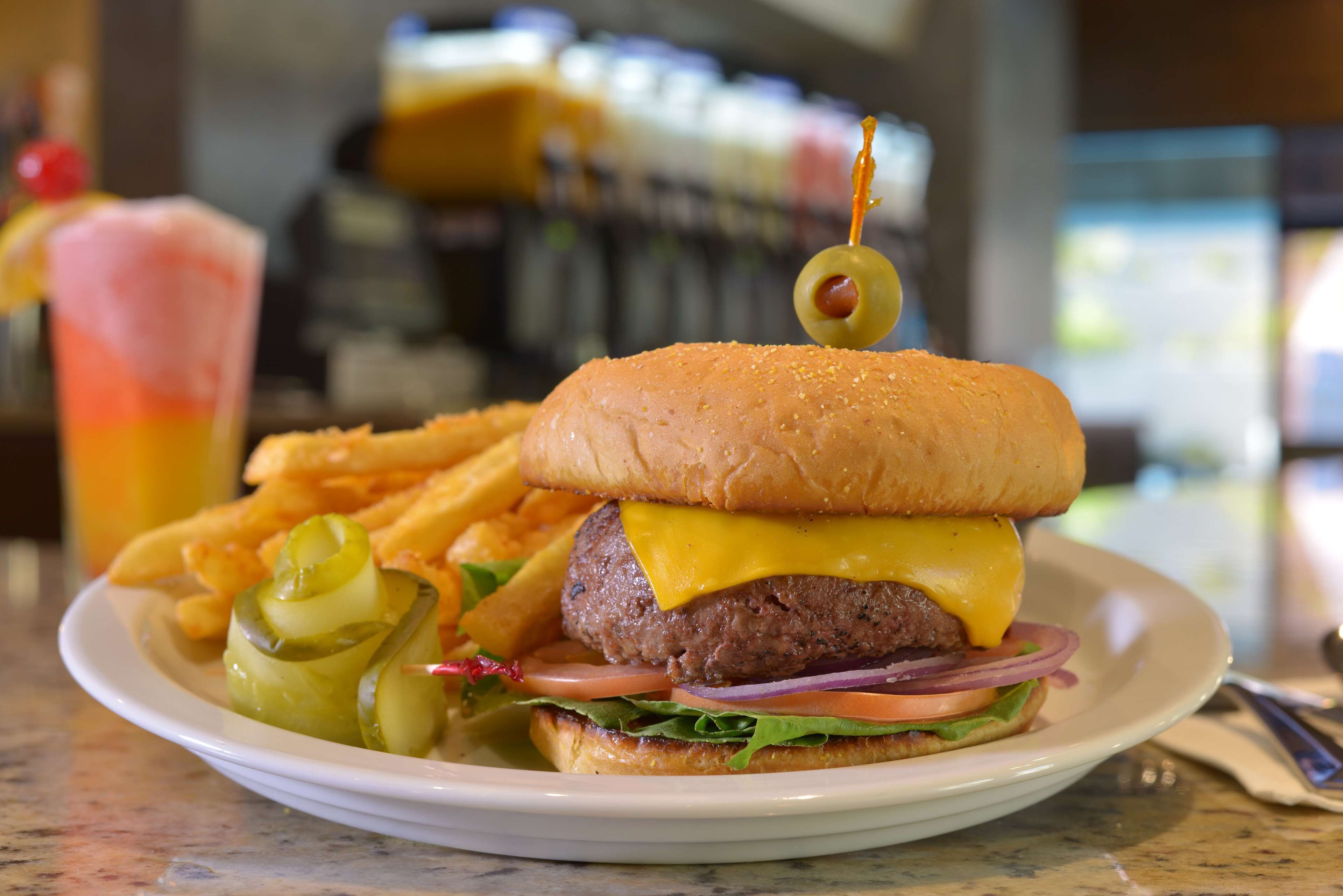 A burger with pickles, cheese, and a toothpick on a plate, accompanied by fries.