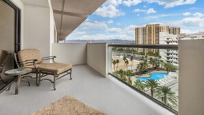 A balcony with a chair and table, overlooking a swimming pool and buildings.