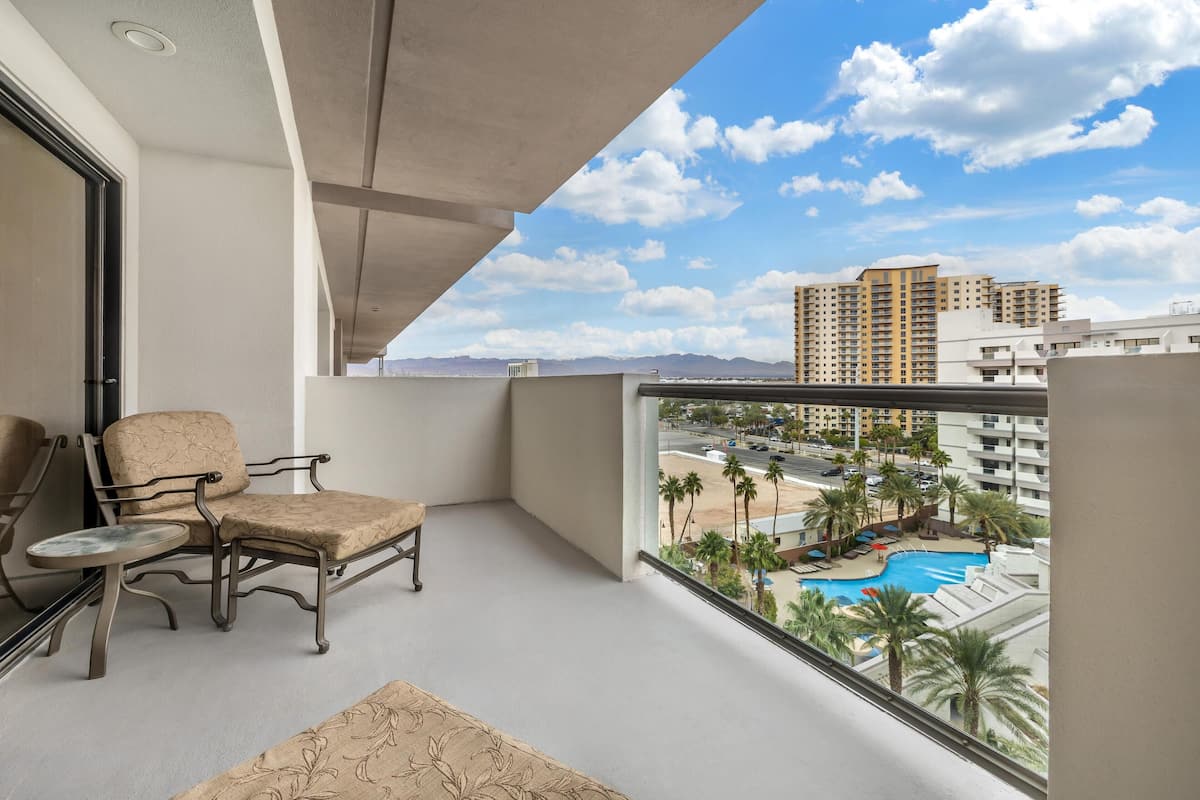 Un balcon avec une chaise et une table, donnant sur une piscine et des immeubles.