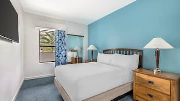 A hotel room with a large bed, two bedside tables with lamps, a window with curtains, and a mirror.