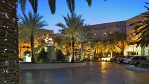 A hotel courtyard with palm trees, a pool, and a building with multiple floors and balconies.