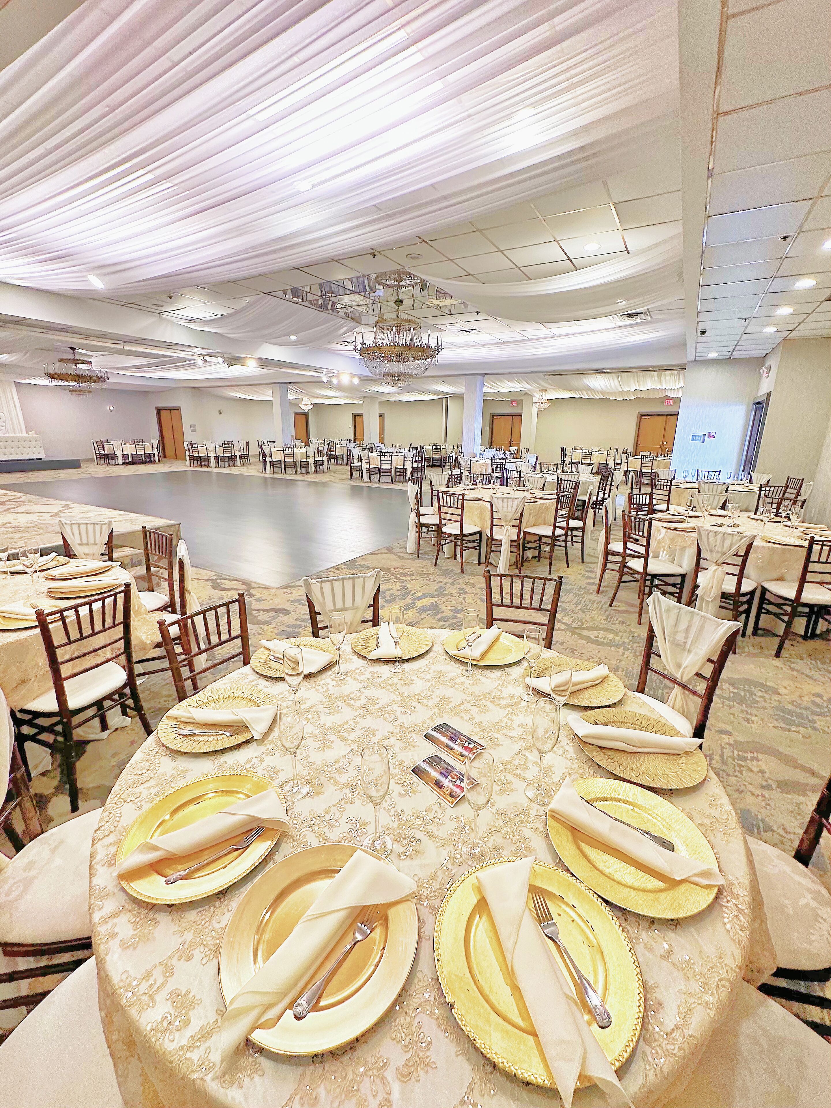 Un salón de banquetes con mesas redondas dispuestas para un evento formal, con candelabros y una amplia pista de baile central.