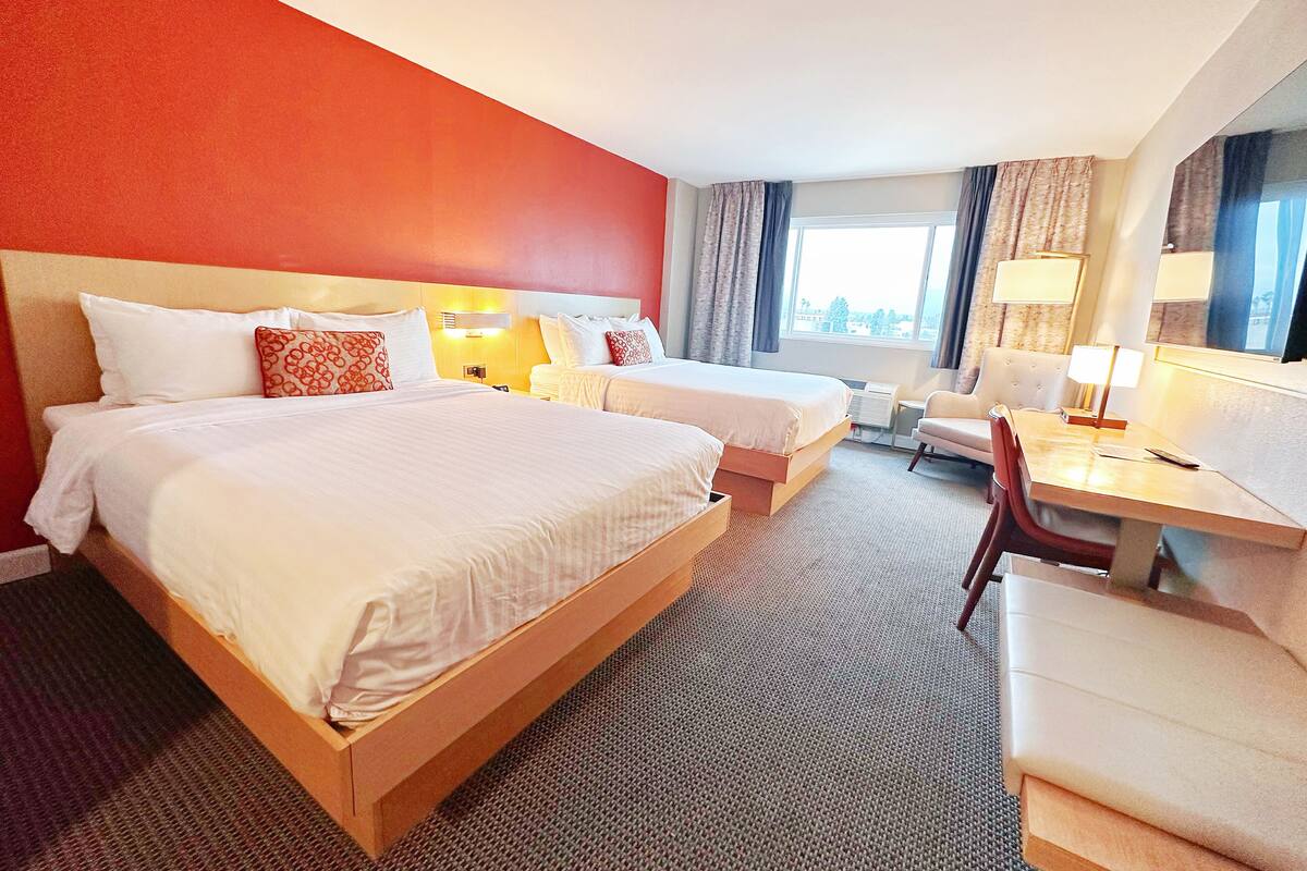 A hotel room with two beds, a desk, a chair, and a large window.