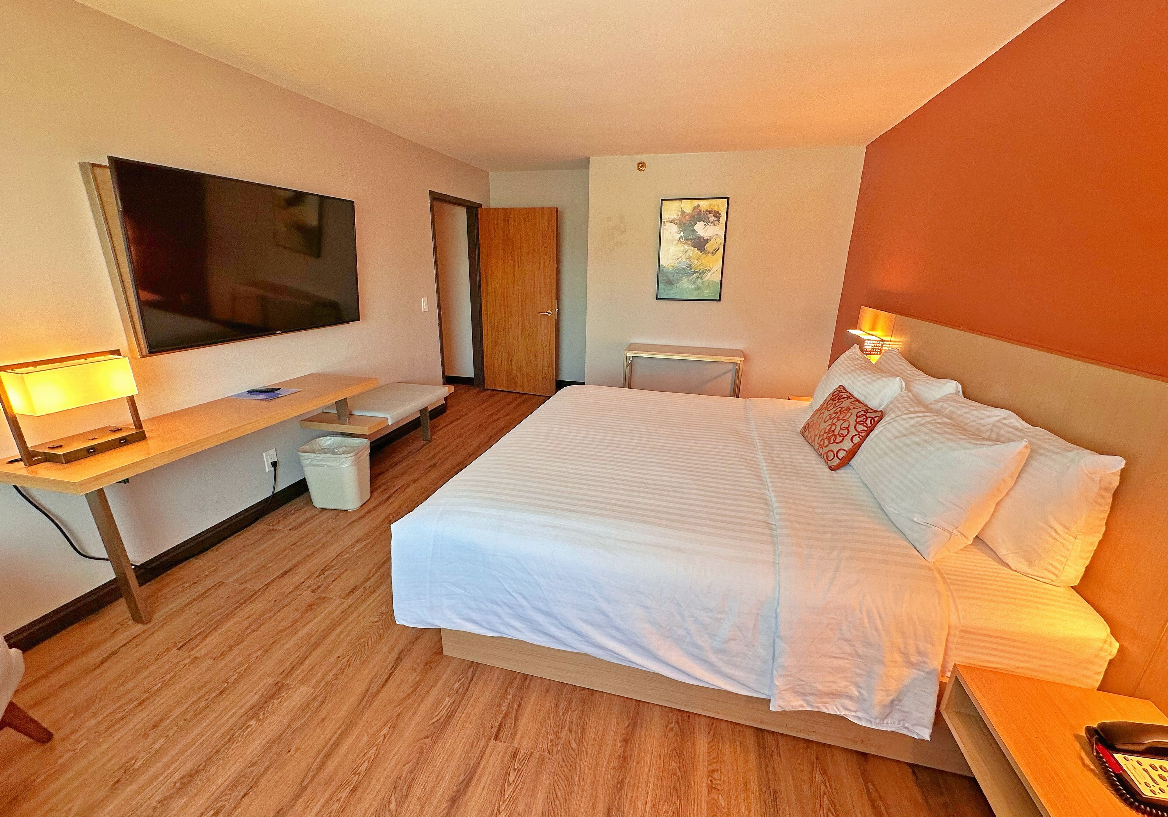 A hotel room with a large bed, a TV, a desk, and a bedside table.