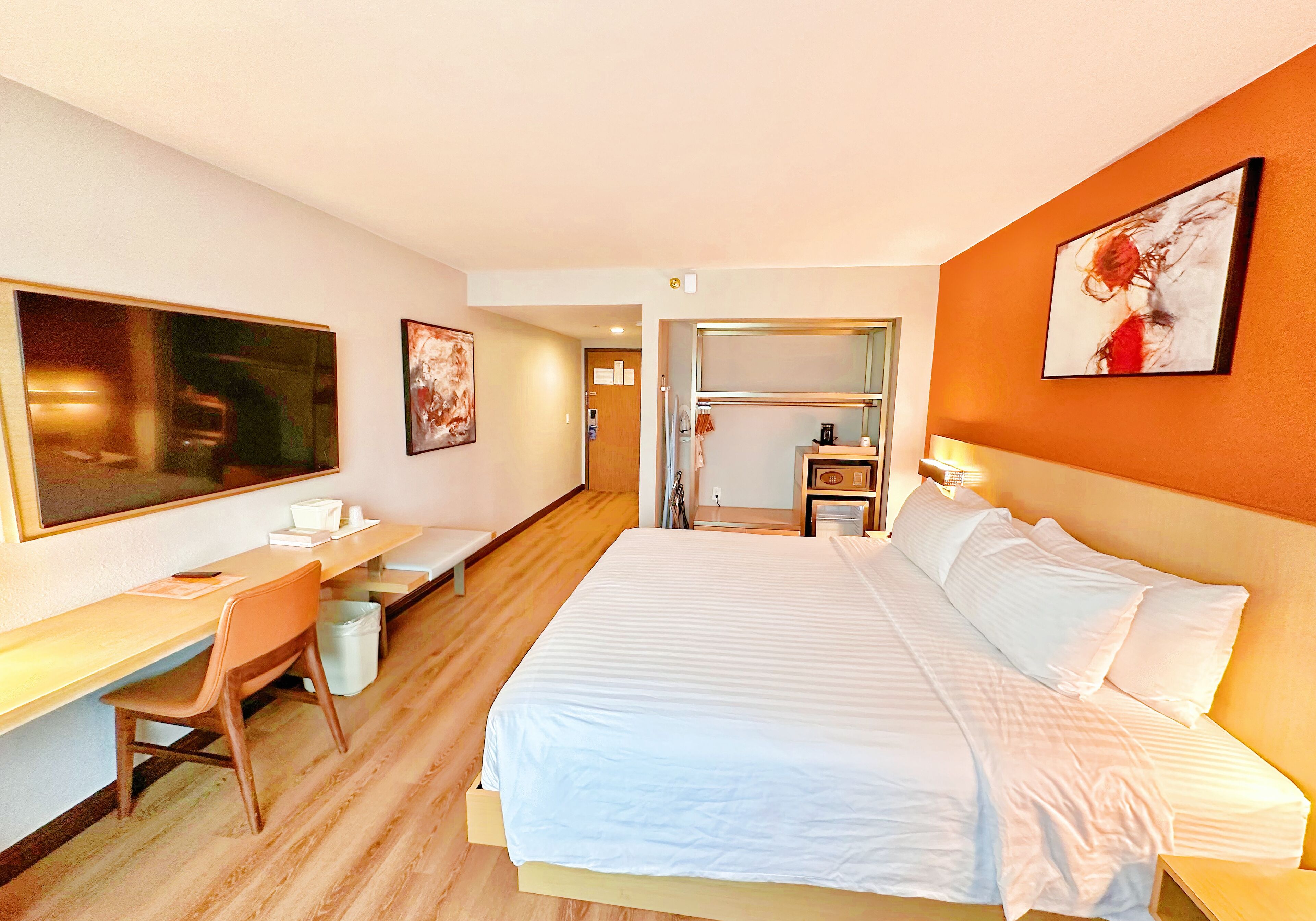 A hotel room with a large bed, a desk with a chair, a small table, and a nightstand.