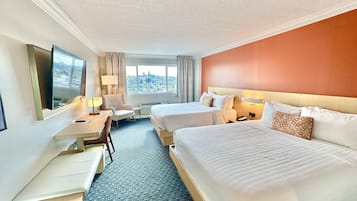 A hotel room with two beds, a desk, a chair, a TV, and a window with a city view.