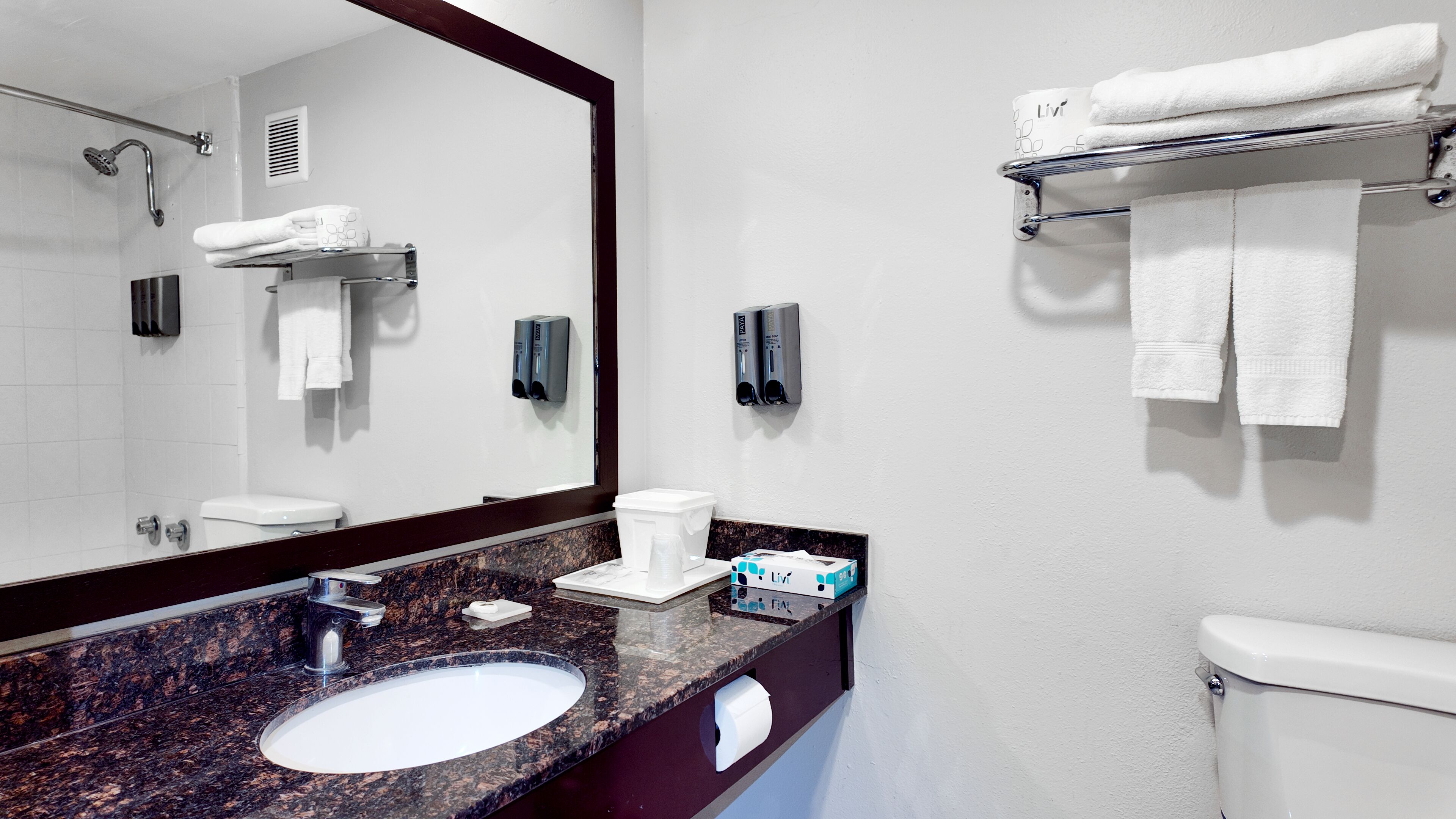 A bathroom with a sink, mirror, towel rack, toilet, and hand dryer.