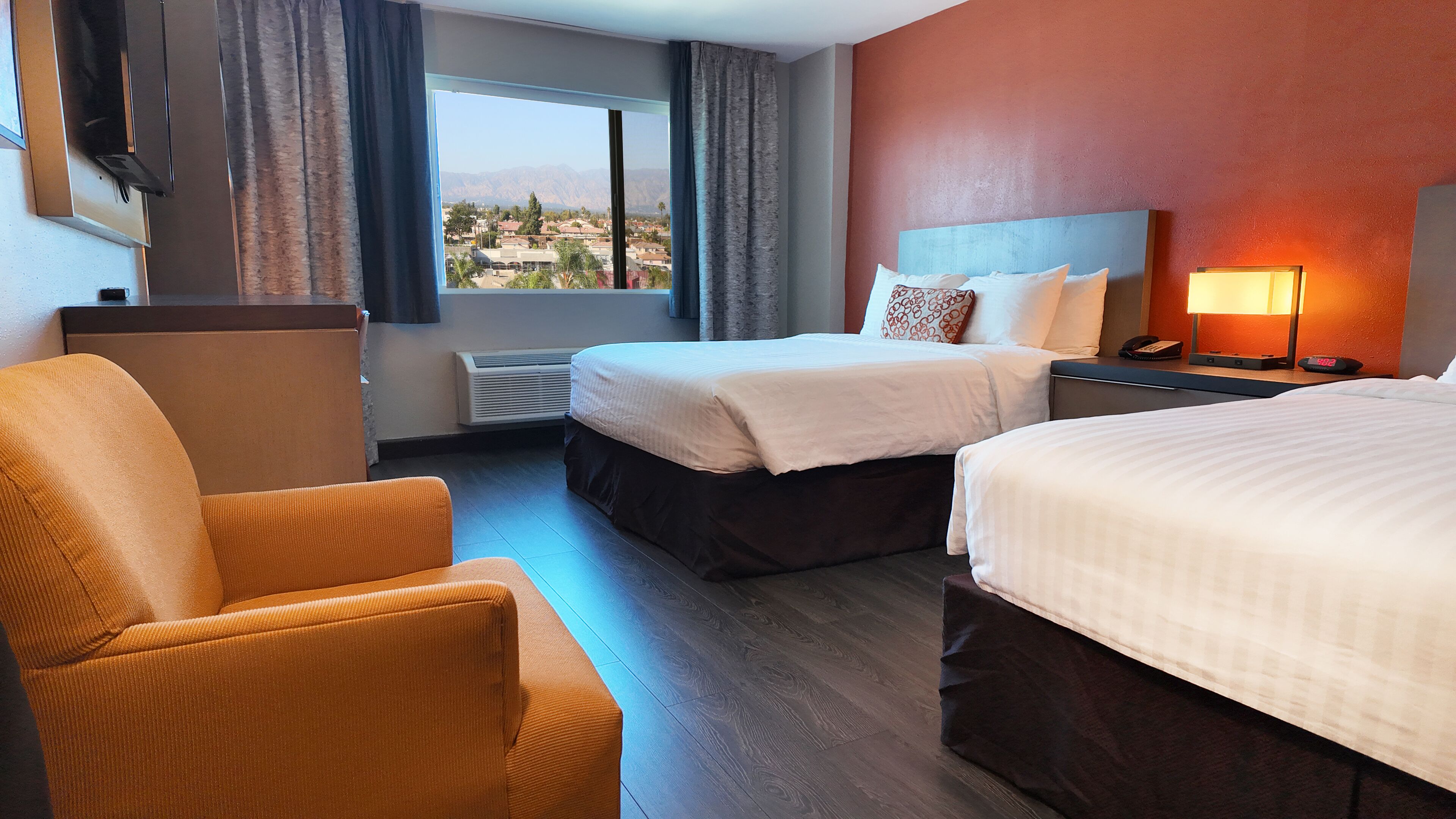 Habitación de hotel con dos camas, un sofá, un escritorio con lámpara y vistas a las montañas.