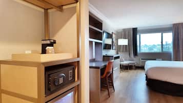Habitación de hotel con cama, escritorio, silla y cafetera sobre un estante de madera.